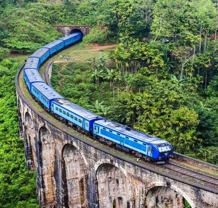 Blue passenger train crossing the Nine Arch Bridge amid green hills, shown by Acme Travels
