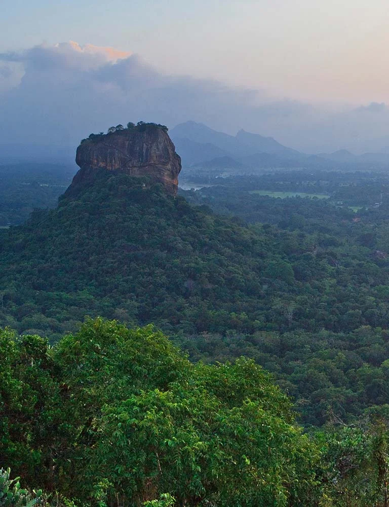 Sigiriya rock rising above green forest beneath a misty sky