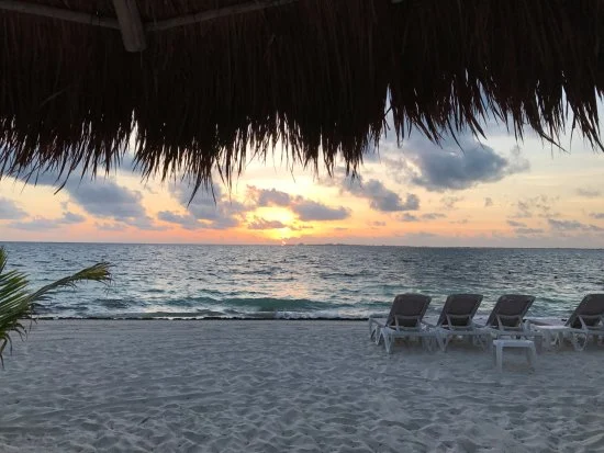 Sun loungers beneath a thatched roof overlooking the sea at sunset