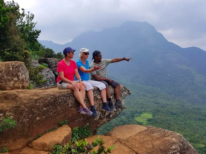 Travellers sitting on a rocky viewpoint above green mountains