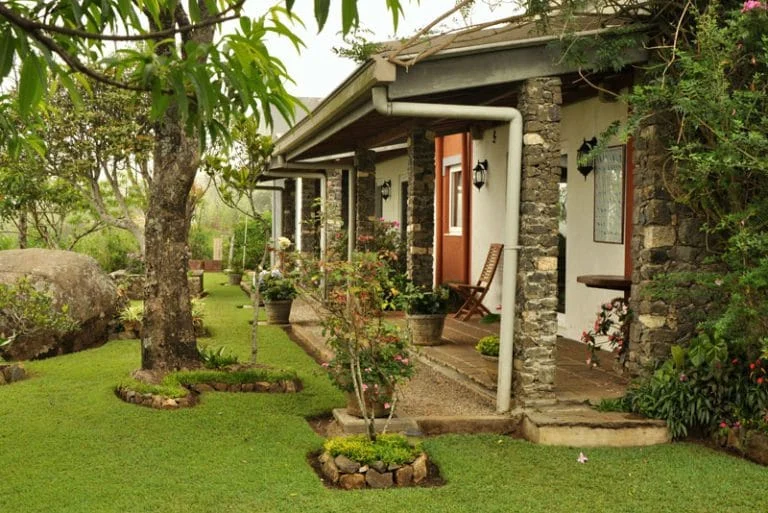 Stone bungalow with a veranda beside a green garden