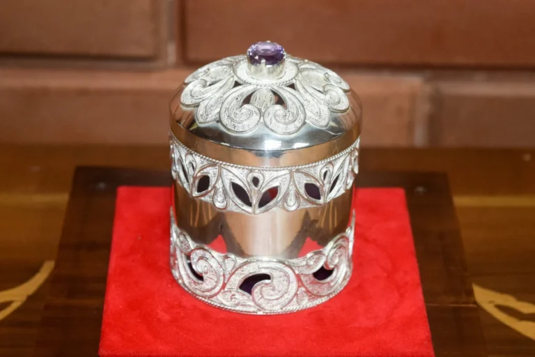 Ornate silver-coloured lidded ornament displayed on a red base at Dienge