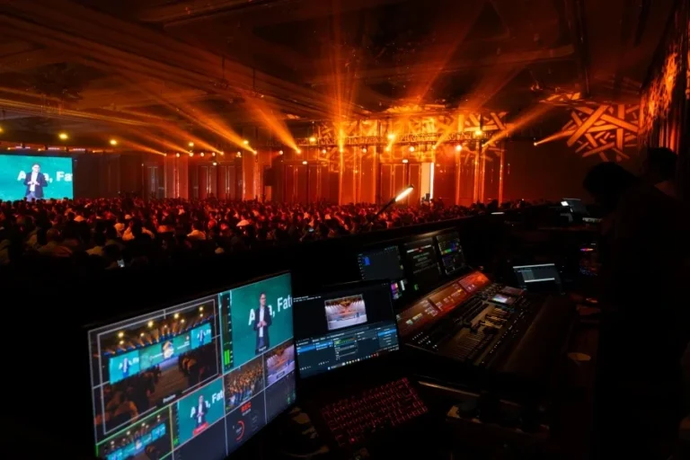 Event stage lit in orange with production control screens in the foreground