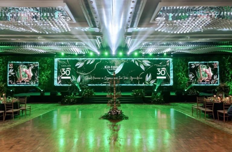 Event venue with a green-lit stage, overhead lighting and seating by Eventz N Trendz