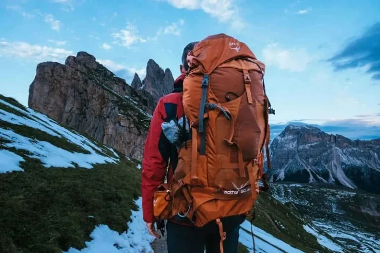 Hiker carrying an orange travel backpack on a mountain trail